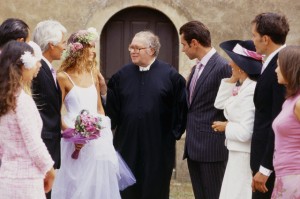 Reverend speaking with newlywed couple, wedding guests standing around